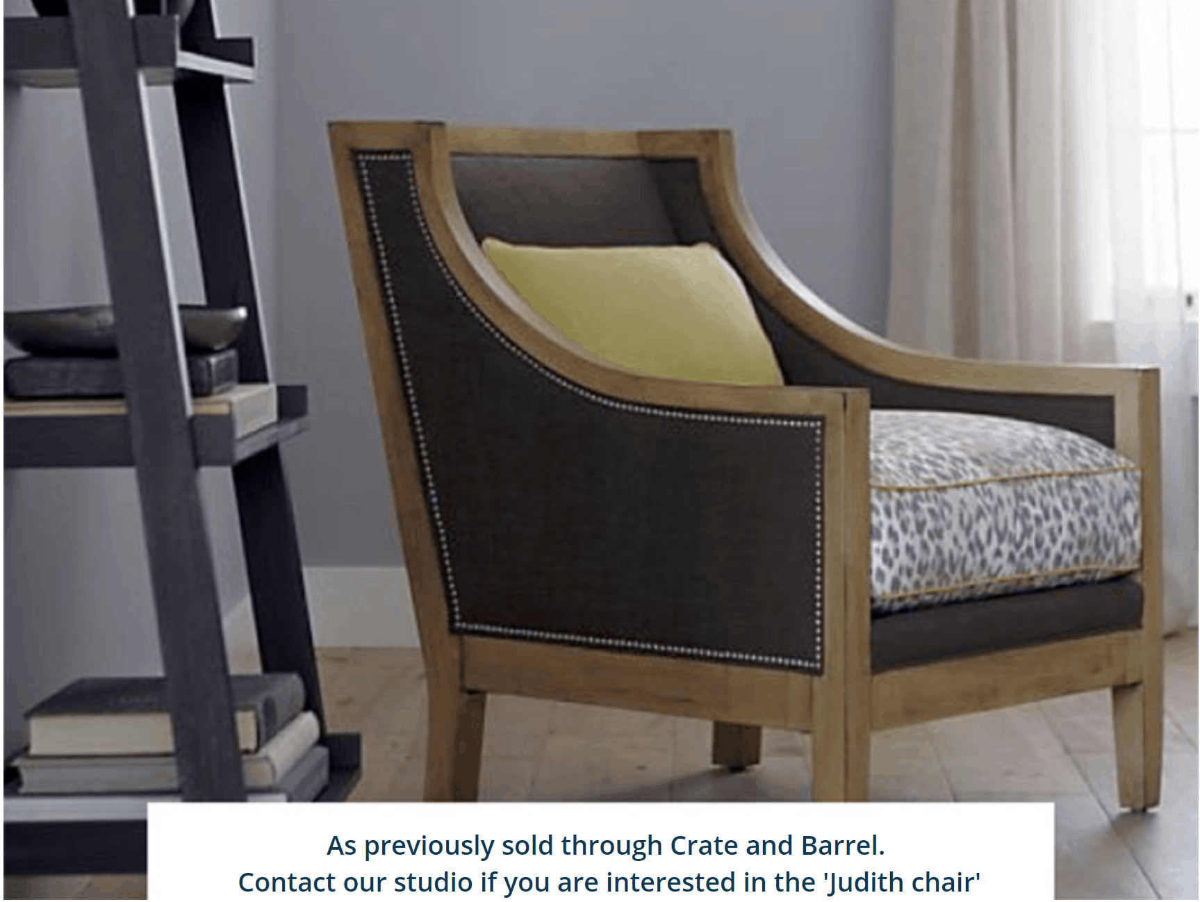 decorative armchair, gray with animal print cushion, yellow pillow. Seated inside room with wood grain shelving