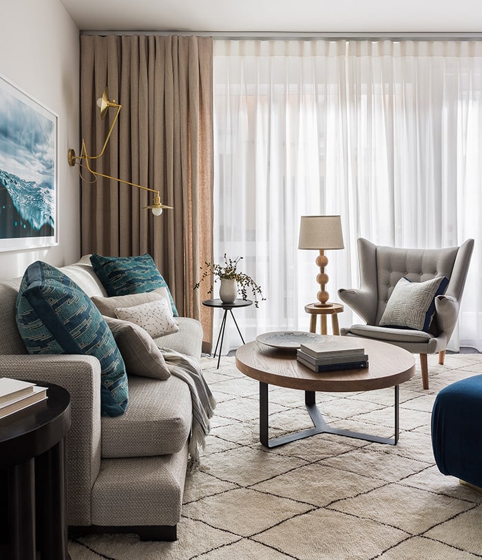 Photo of modern living room with round coffee table, sofa, and teddy bear chair in front of floor to ceiling, wall to wall drapery