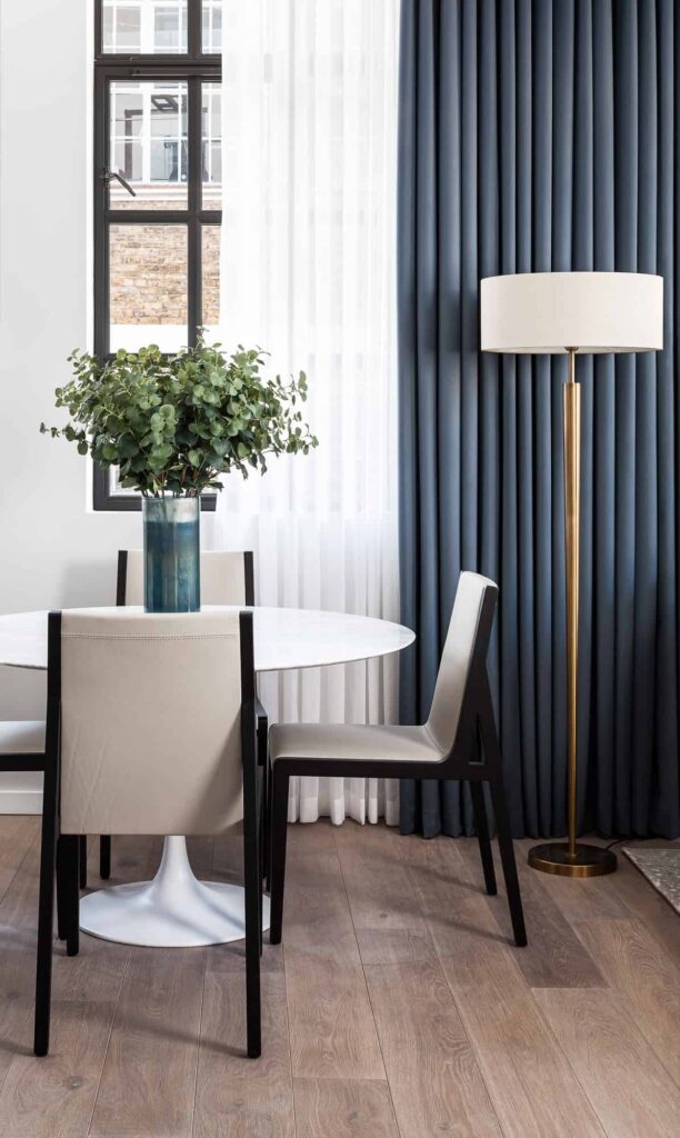 Modern round tulip table with chairs and floor lamp in front of window with white sheers and blue drapes.
