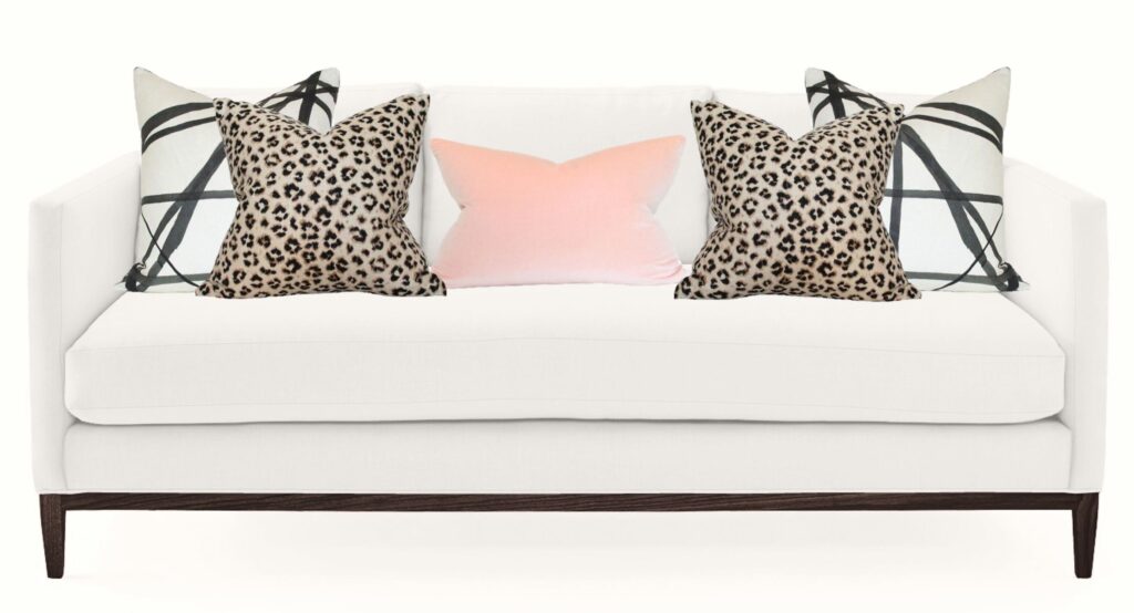 white sofa with geometric and animal print pillows and a pink one in the centre