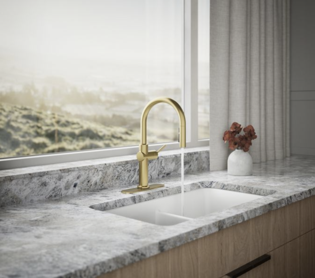 A brushed gold faucet in front of a window with a lovely hazy view