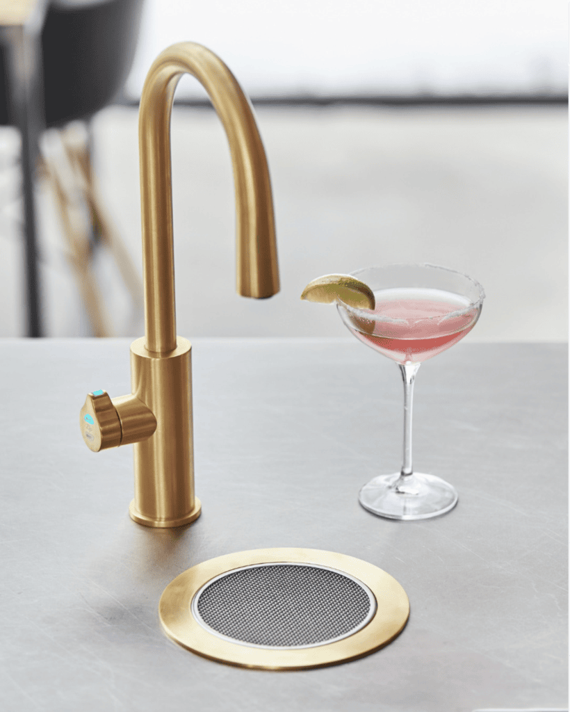 A brushed gold modern faucet next to a pink martini